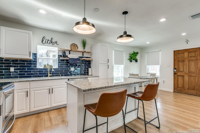 kitchen featuring tasteful backsplash, stainless steel stove, visible vents, light wood-style flooring, and a sink