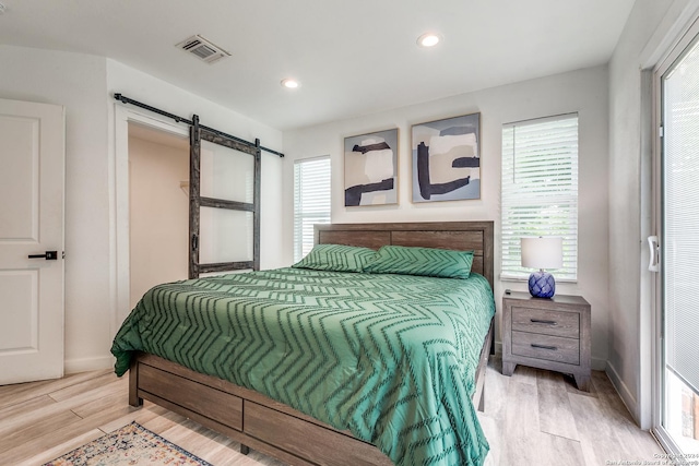 bedroom with a barn door, recessed lighting, wood finished floors, visible vents, and baseboards