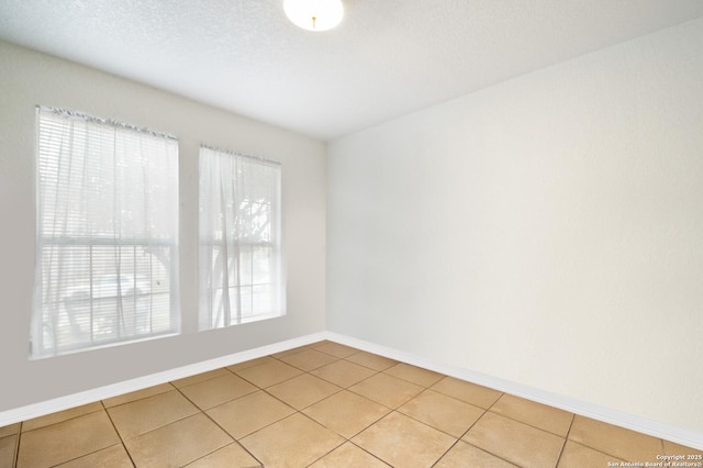 empty room featuring light tile patterned flooring, a textured ceiling, and baseboards