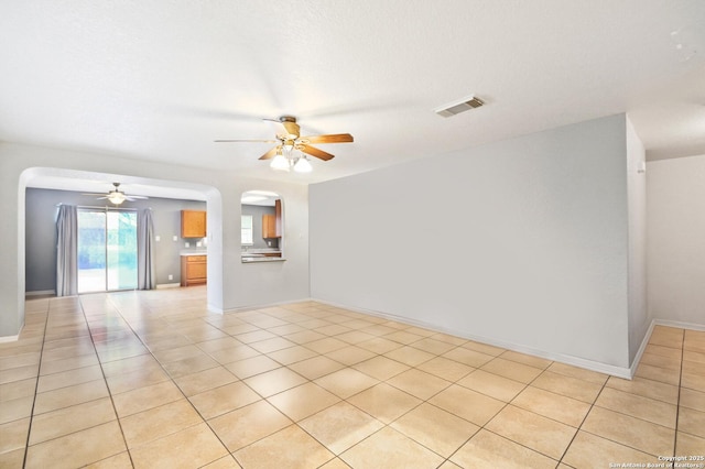 spare room featuring visible vents, arched walkways, baseboards, ceiling fan, and light tile patterned flooring