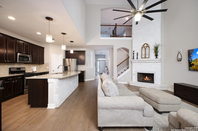 kitchen featuring stainless steel appliances, open floor plan, a sink, dark brown cabinetry, and wood finished floors