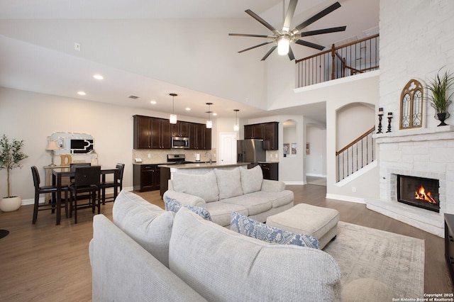 living area with ceiling fan, high vaulted ceiling, a fireplace, baseboards, and light wood-style floors