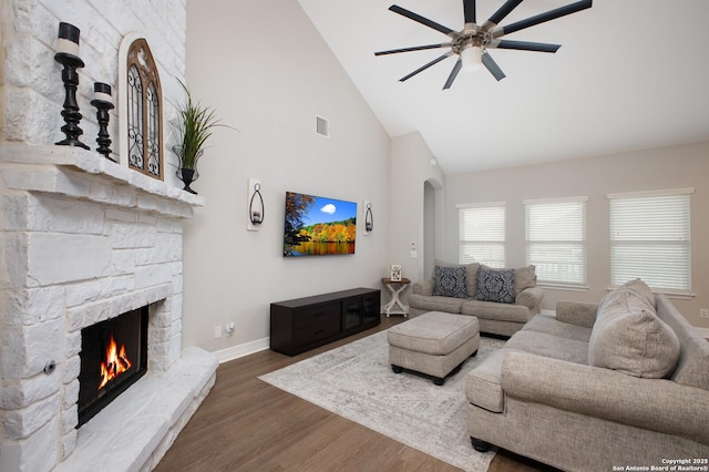 living area featuring a fireplace, visible vents, a ceiling fan, wood finished floors, and high vaulted ceiling