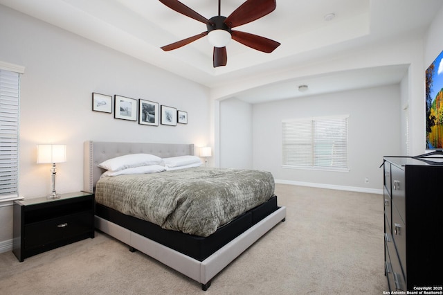 bedroom featuring light carpet, baseboards, a tray ceiling, and ceiling fan