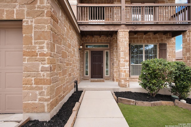 entrance to property with a garage, a balcony, and stone siding