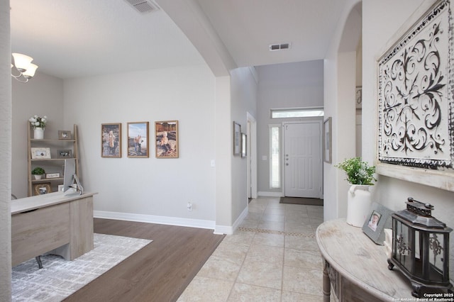 foyer with baseboards, visible vents, arched walkways, and wood finished floors