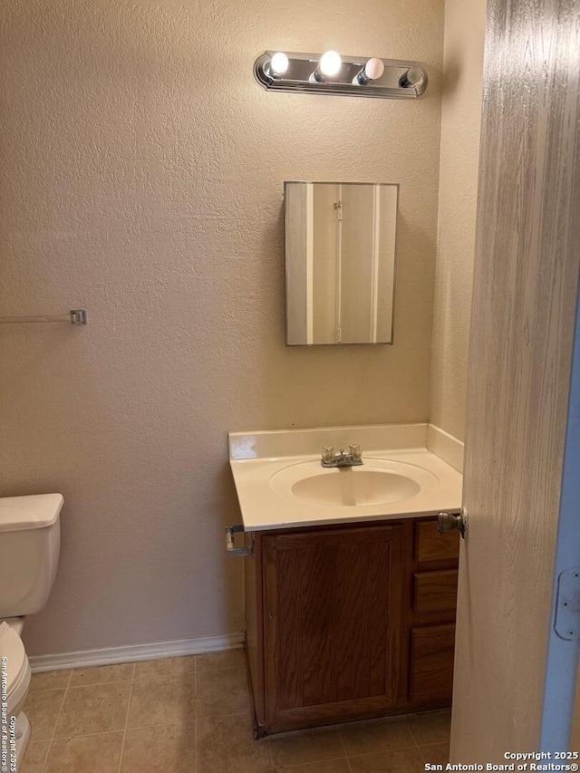 half bath featuring baseboards, vanity, toilet, and tile patterned floors