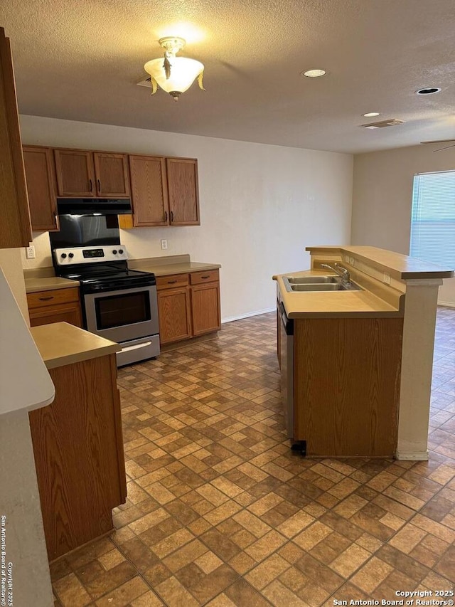 kitchen with light countertops, appliances with stainless steel finishes, brown cabinetry, a sink, and under cabinet range hood