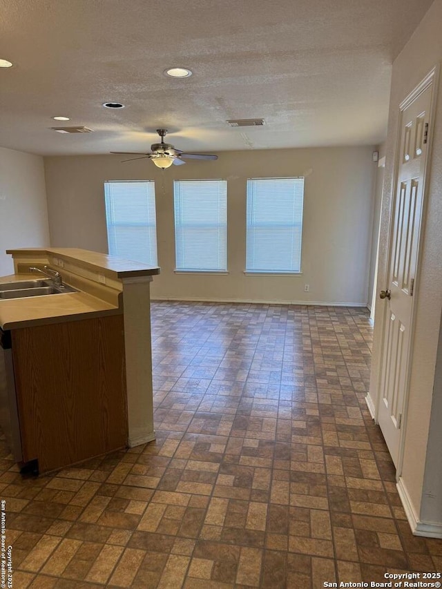 kitchen with brick floor, visible vents, a ceiling fan, a sink, and baseboards