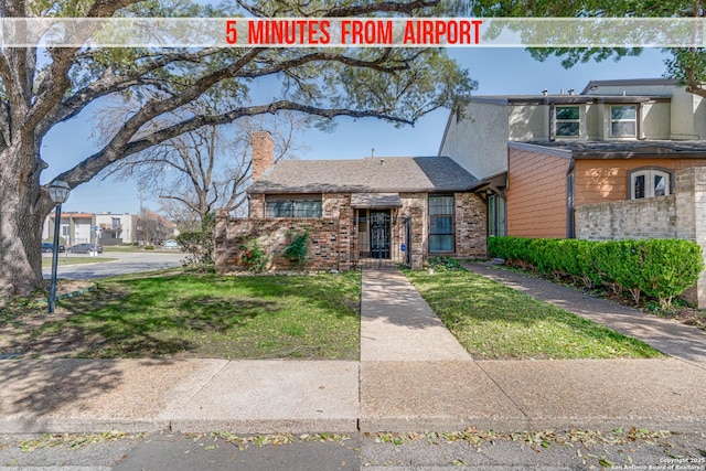 view of front of house with a shingled roof, brick siding, a chimney, and a front lawn