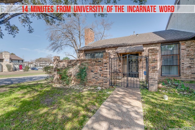 exterior space with a chimney, a gate, fence, a front lawn, and brick siding