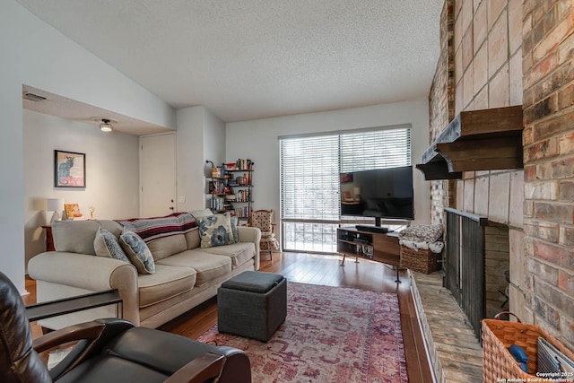 living area featuring a textured ceiling, a fireplace, visible vents, and wood finished floors