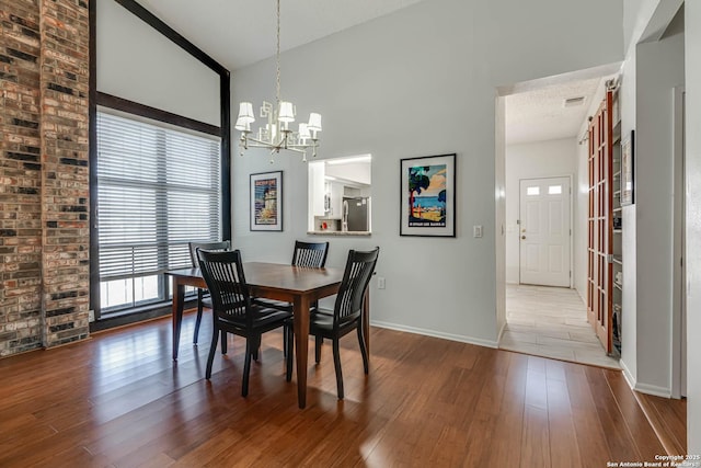 dining area with a chandelier, wood-type flooring, baseboards, and a high ceiling