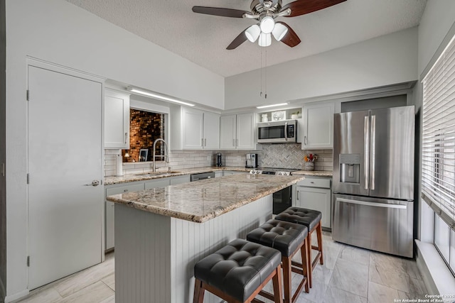 kitchen with a kitchen island, a sink, appliances with stainless steel finishes, backsplash, and a kitchen bar