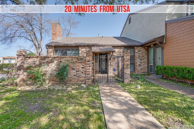 view of front of house with a chimney, roof with shingles, a gate, fence, and brick siding