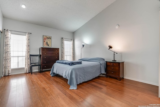 bedroom featuring vaulted ceiling, a textured ceiling, baseboards, and wood finished floors