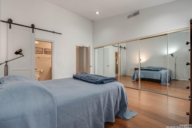 bedroom with a barn door, visible vents, a towering ceiling, wood finished floors, and ensuite bathroom