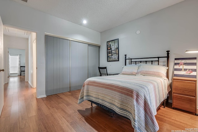 bedroom with attic access, light wood-type flooring, a closet, and a textured ceiling