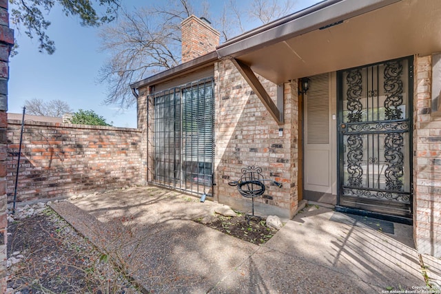 entrance to property with brick siding, a chimney, and fence