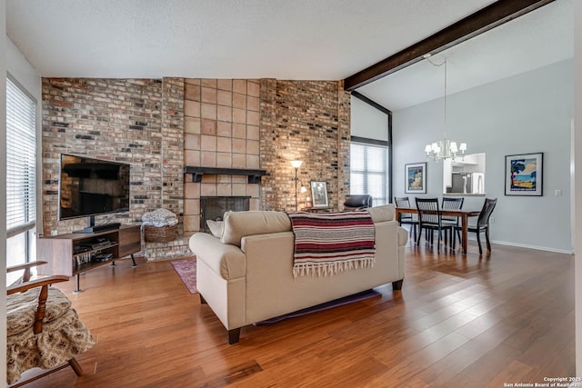 living area with wood finished floors, vaulted ceiling with beams, a textured ceiling, a fireplace, and a chandelier