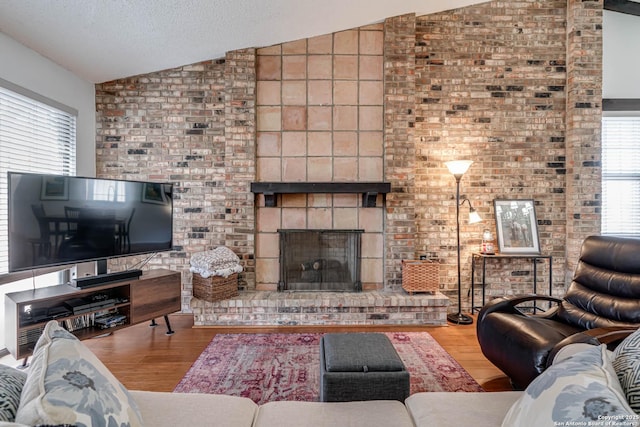 living room with a brick fireplace, vaulted ceiling, a textured ceiling, and wood finished floors