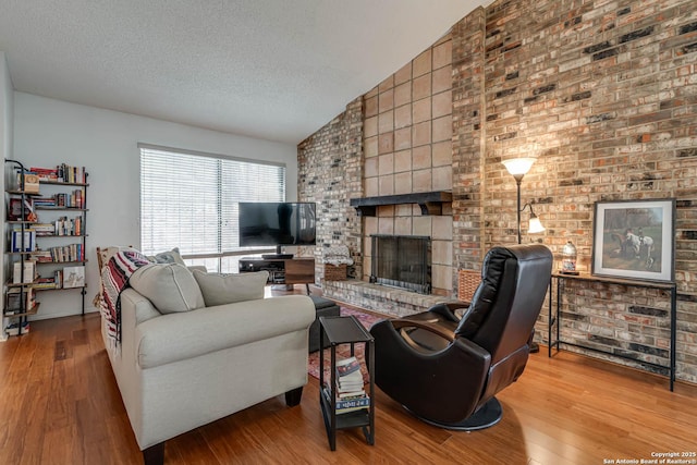 living area with a brick fireplace, vaulted ceiling, a textured ceiling, and wood finished floors