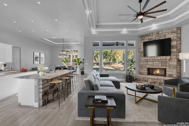 living area featuring a fireplace, recessed lighting, a raised ceiling, ceiling fan, and light wood-type flooring