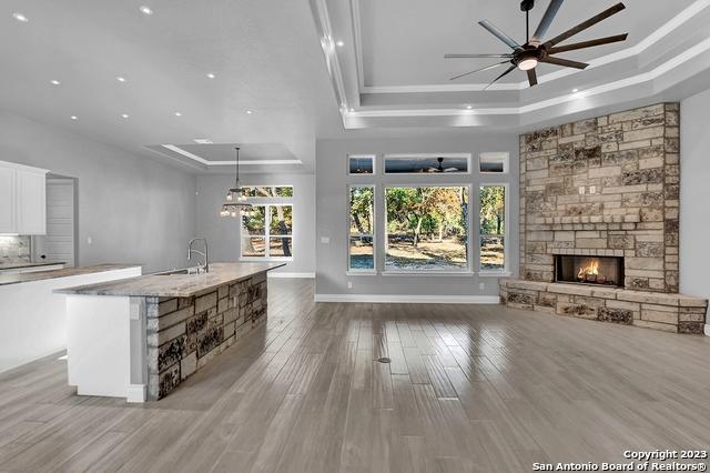 unfurnished living room with a ceiling fan, wood finished floors, a tray ceiling, a stone fireplace, and a sink