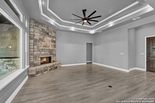 unfurnished living room with a raised ceiling, visible vents, a stone fireplace, and wood finished floors