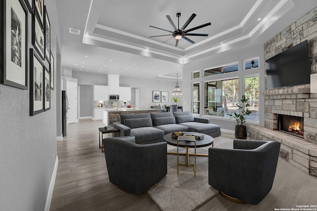 living area with a tray ceiling, a fireplace, visible vents, wood finished floors, and baseboards