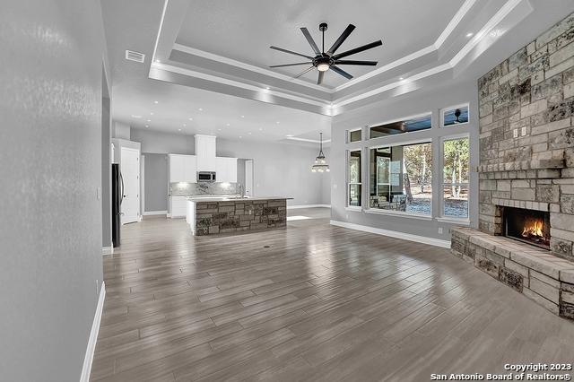 unfurnished living room with dark wood-type flooring, a fireplace, a raised ceiling, and crown molding