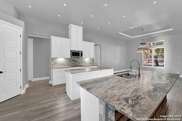 kitchen featuring wood finished floors, a sink, a large island, a tray ceiling, and stainless steel microwave