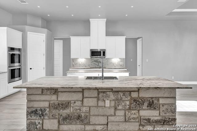 kitchen with light stone counters, stainless steel appliances, white cabinetry, a sink, and a large island with sink