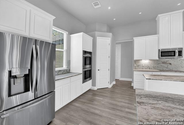 kitchen with tasteful backsplash, visible vents, white cabinets, light stone counters, and stainless steel appliances