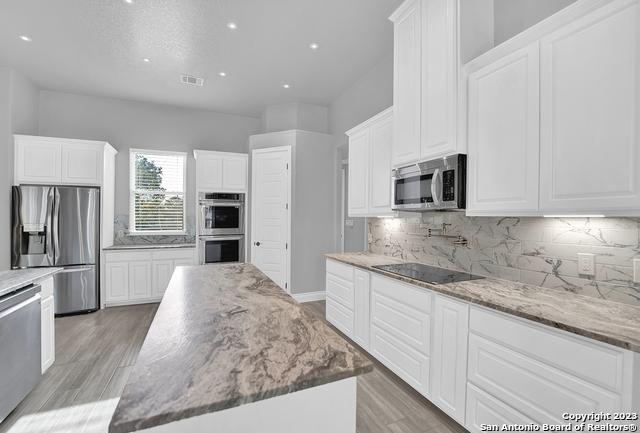 kitchen featuring appliances with stainless steel finishes, light wood-style flooring, white cabinets, and tasteful backsplash