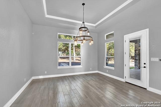 unfurnished dining area with a tray ceiling, dark wood finished floors, baseboards, and an inviting chandelier