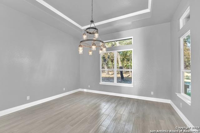 unfurnished dining area with baseboards, a raised ceiling, ornamental molding, wood finished floors, and a notable chandelier