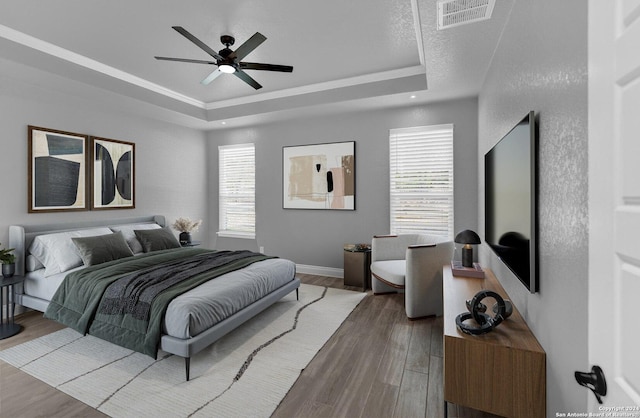 bedroom featuring wood finished floors, a raised ceiling, visible vents, and baseboards