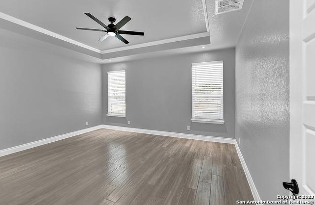 empty room featuring wood finished floors, a raised ceiling, visible vents, and baseboards