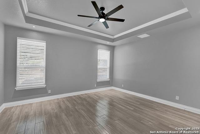 empty room featuring baseboards, a raised ceiling, and wood finished floors