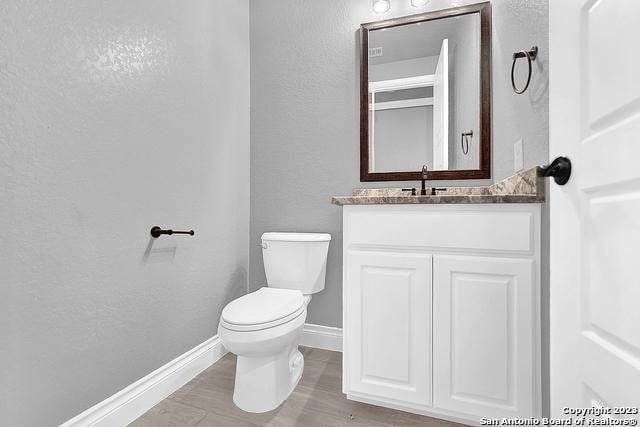 half bathroom featuring toilet, baseboards, wood finished floors, and vanity