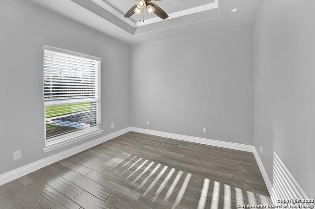 empty room with baseboards, a tray ceiling, ceiling fan, and wood finished floors