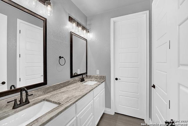 full bath with double vanity, wood finished floors, and a sink