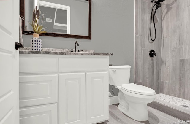 full bathroom featuring a tile shower, vanity, and toilet