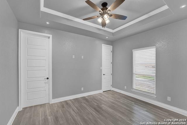 empty room with baseboards, a tray ceiling, and wood finished floors