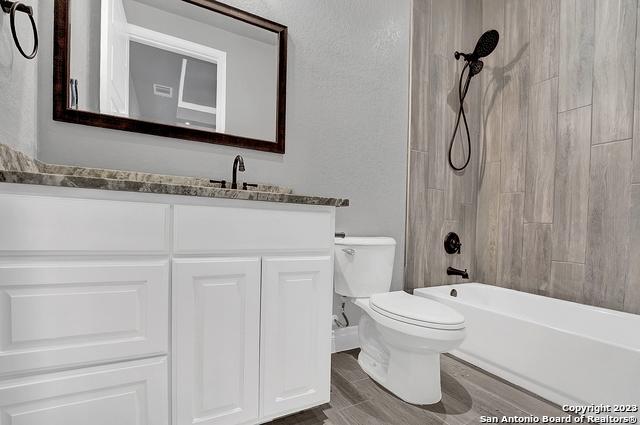 full bath featuring shower / bathtub combination, a textured wall, toilet, wood finished floors, and vanity