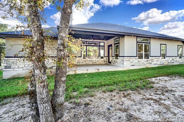 rear view of house with ceiling fan, a patio, stone siding, a lawn, and stucco siding