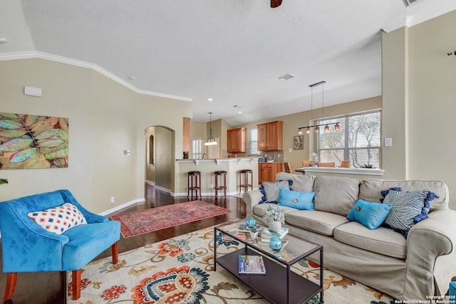 living room with arched walkways, crown molding, vaulted ceiling, wood finished floors, and baseboards