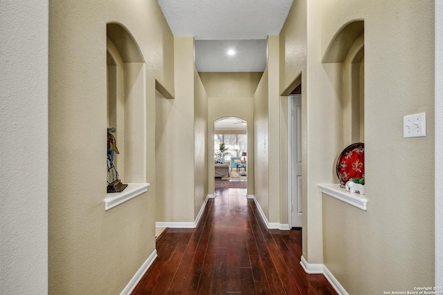 hallway featuring arched walkways, baseboards, and wood finished floors