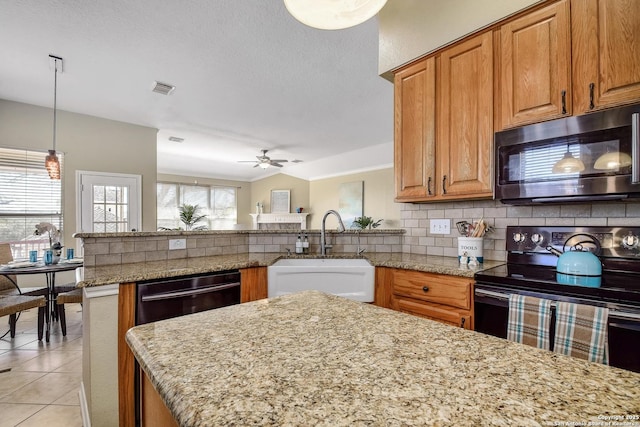 kitchen featuring tasteful backsplash, stainless steel microwave, black range with electric stovetop, a sink, and light stone countertops